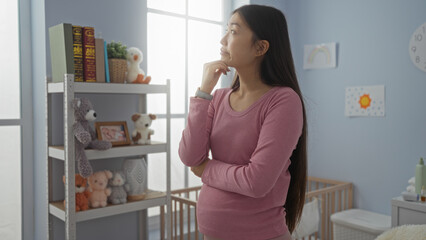 Pregnant woman in bedroom stands thinking next to crib surrounded by stuffed animals and baby decor