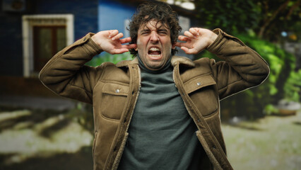 Frustrated man outdoors on city street covering ears with hands portraying annoyance and discomfort in urban environment.