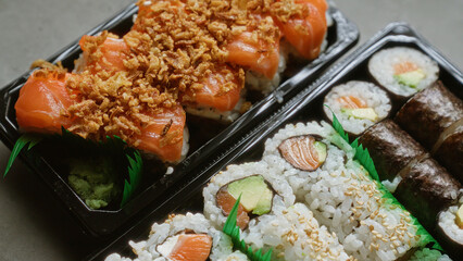 Delicious sushi rolls with salmon avocado seaweed and garnish in black trays closeup