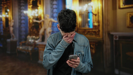 Man using smartphone indoors with ornate background looking engaged and thoughtful in elegant urban setting.