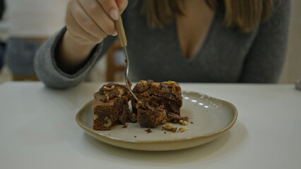 Woman enjoying dessert in luxurious modern restaurant cafeteria, showcasing elegance and culinary delight with chocolate brownie and fork close-up.