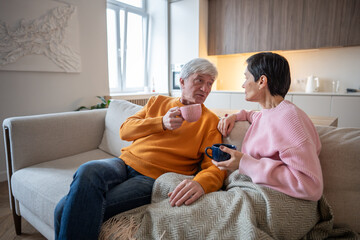 Delighted engaged husband and wife talking discussing stories while seated on couch. Interested spouses on tea break sharing with each other, having conversation together, rest relax at home