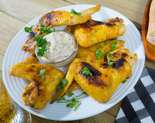 Crispy fried chicken wings on white plate with creamy mustard sauce and greens..