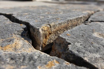 Close-up view of weathered stone paving with textured surface, displaying visible cracks and signs of aging, capturing the essence of time and natural elements.