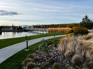 Obraz premium Beautiful landscaped park with wooden bridge over calm reflective water in daylight