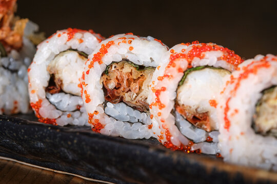 Sushi rolls with red tobiko caviar and tempura shrimp filling resting on a wooden serving tray