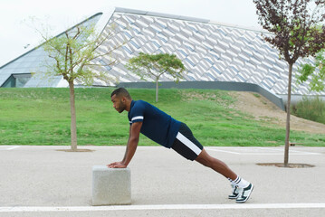 Athletic black male training outdoors with push-ups