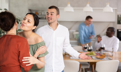 Two women friends greet each other when meeting at party in kitchen