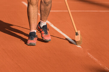 Man cleans tennis line on clay court with a broom