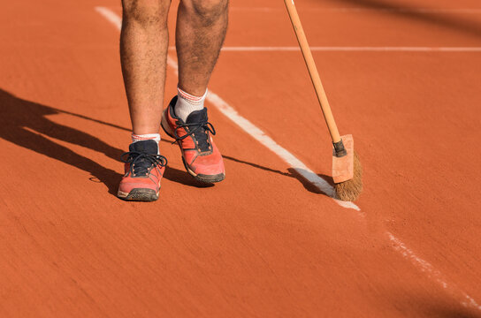 Man cleans tennis line on clay court with a broom