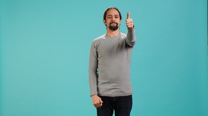 Portrait of upbeat man showing thumbs up sign gesturing, exulting happy facial expression and satisfaction. Jolly Arab person being excited, doing approving hand gesture, studio background, camera A
