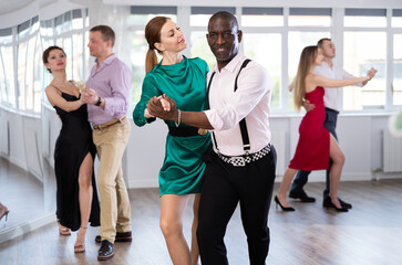 Fototapeta premium With unhurried music, woman with African man in couple spins to rhythm of waltz during lesson for novice students. Classes in mini-groups for those who want to learn dancing