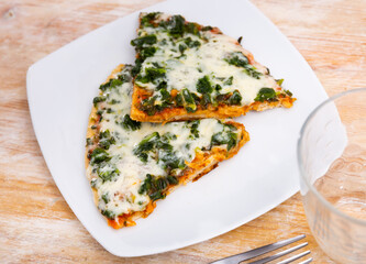Restaurant serves portion of spinach pizza - triangular slices and glass of red wine. Pizza made according to traditional Italian recipe from fresh spinach leaves, large amount of young white cheese