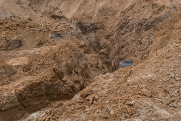An excavation site at a construction area with a concrete ring installed, intended for utilities or drainage. Piles of loose soil and exposed layered rocks create a textured, natural background.
