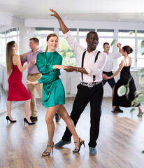 Dynamic middle-aged male and female attendees of dancing courses doing waltz in group