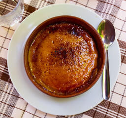 Crema catalana - dessert of Catalonia served with spoon in clay bowl on table in cafe. Spanish dish