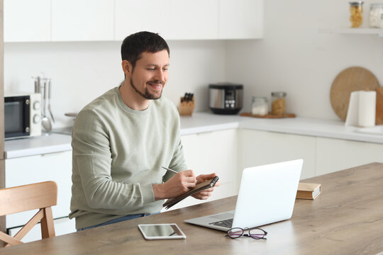 Young male teacher with laptop and notebook giving online lesson at home
