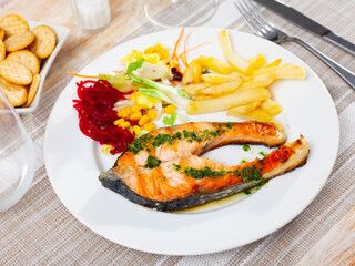 Baked salmon served with potatoes and fresh vegetable salad on plate..