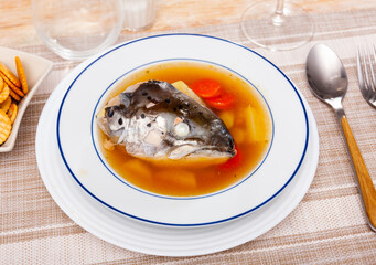 Delicious homemade fish broth with salmon head and vegetables served with crispy salty crackers..