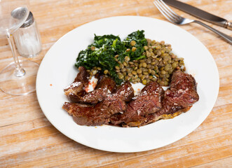 Delicious fried beef pieces served with spinach and lentils on plate