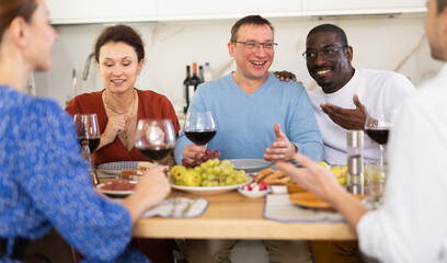 Merry male and female friends having lunch with wine and talking warmly in comfort of their house