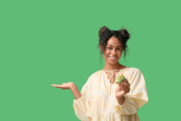 African-American woman with tasty eclair showing something on green background