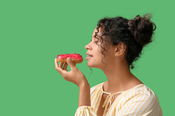African-American woman eating tasty eclair on green background
