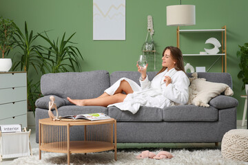 Young woman in bathrobe with glass of water lying on sofa at home