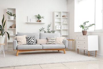 Interior of light living room with grey sofa, commode and shelf units