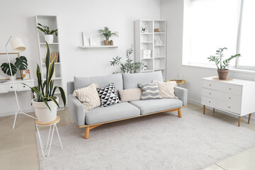 Interior of light living room with grey sofa, commode and shelf units