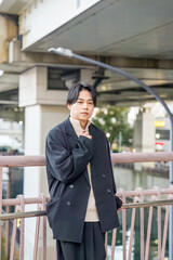 A Japanese man in his twenties wearing a black jacket is in Minato Mirai, Yokohama, Kanagawa Prefecture. He sits on a bench, gazing into the distance, surrounded by the calm mood of the modern city.