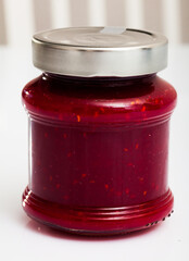 Tasty sweet raspberry jam in closed glass jar on white surface..