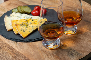 Whiskey and cheese pairing, tasting whisky glasses and plate with sliced crumbly old blue stilton and blue shropshire cheeses, Great Britain food and drink