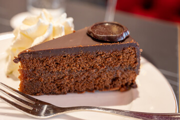 Piece of famous Sachertorte chocolate cake with apricot jam of Austrian origin served with whipped cream in old classic cafe-restaurant in Vienna
