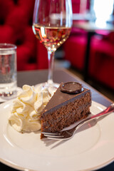 Piece of famous Sachertorte chocolate cake with apricot jam of Austrian origin served with whipped cream in old classic cafe-restaurant in Vienna