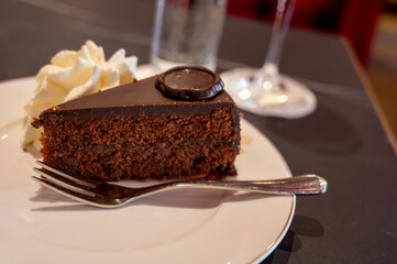 Piece of famous Sachertorte chocolate cake with apricot jam of Austrian origin served with whipped cream in old classic cafe-restaurant in Vienna