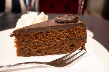 Piece of famous Sachertorte chocolate cake with apricot jam of Austrian origin served with whipped cream in old classic cafe-restaurant in Vienna