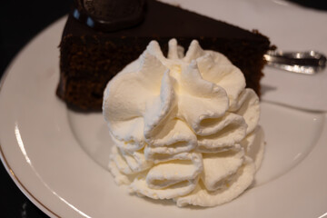 Piece of famous Sachertorte chocolate cake with apricot jam of Austrian origin served with whipped cream in old classic cafe-restaurant in Vienna