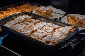 Austrian desserts, just baked whole apple strudel cutted in pieces in kithen of old traditional bakery cafe in Vienna, close up