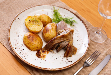 Fried lamb hip and pieces of potato dished up in a plate on the laid restaurant table
