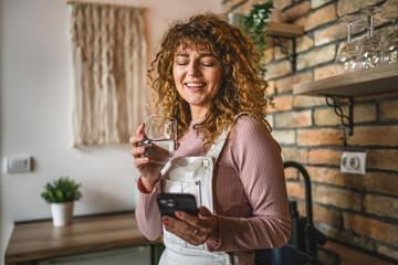 relax curly hair woman use mobile phone while drink water at kitchen