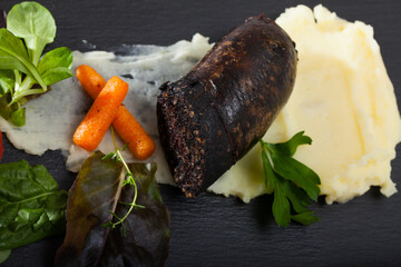Delicious blood sausage with garnish of mashed potatoes, carrots, tomatoes and greens
