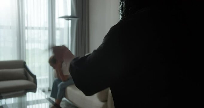 The mother angrily shouts at her teenage daughter. Video in 4K. Domestic violence. A mother raises her hand towards her child, who sits on the sofa, covering their face and closing their eyes in fear.