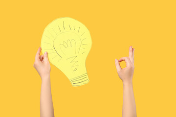 Female hands with paper light bulb showing OK on yellow background