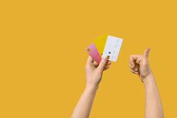 Female hands with credit cards showing thumb-up on yellow background