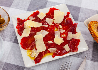 Delicious beef carpaccio with grated hard cheese served on plate. Meat appetizer..