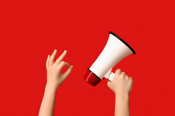 Female hands with megaphone showing OK on red background