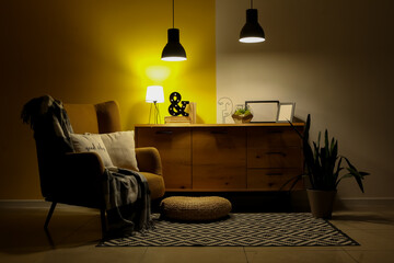 Interior of dark living room with armchair, commode and glowing lamps