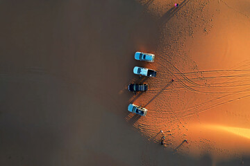 Aerial, overhead view of trucks and tourists at sunrise in the Sahara desert 