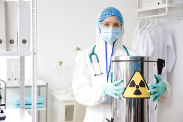 Medical worker in protective uniform and with container for radioactive waste in clinic